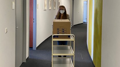 Eine Mitarbeiterin schiebt einen Aktenwagen über den Flur