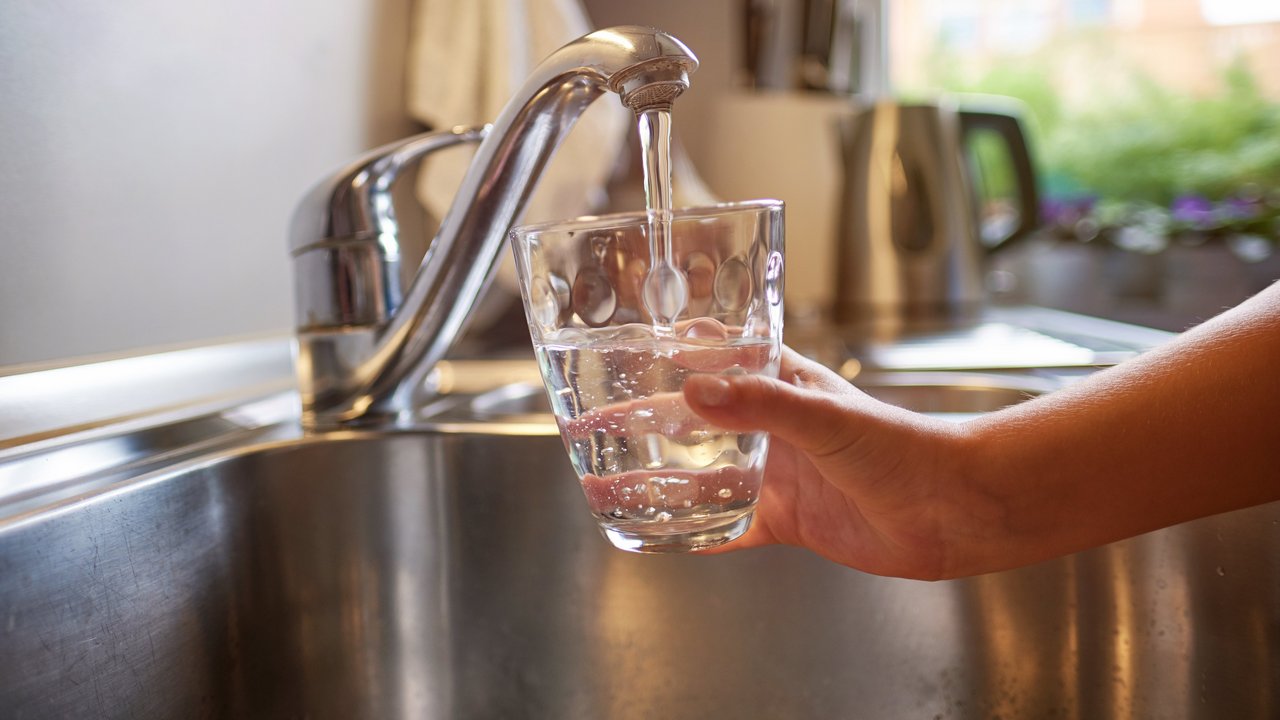 Kinderhand, die sich am Wasserhahn frisches Wasser in ein Glas gießt