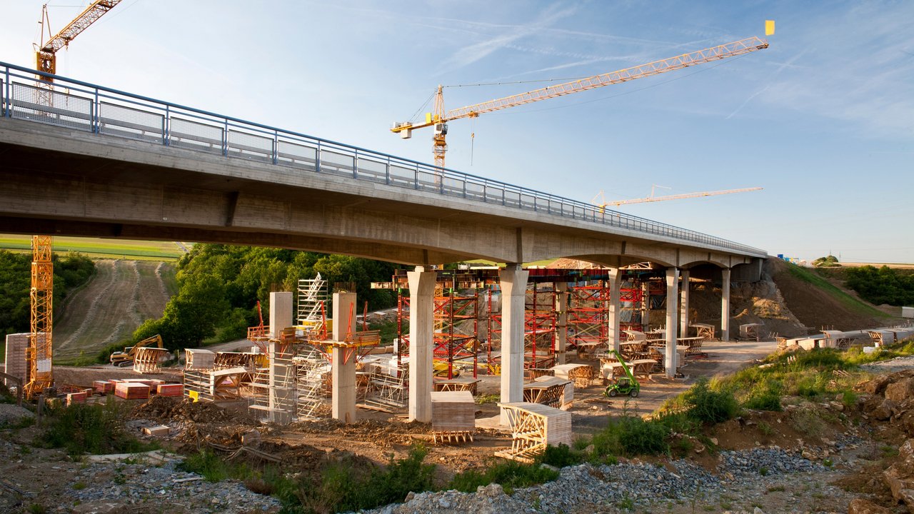 2 Kräne stehen hinter einer Brücke, die saniert werden soll
