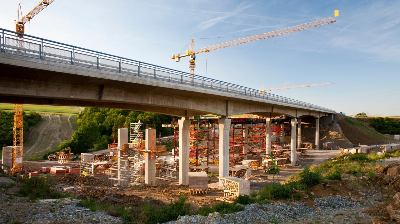2 Kräne stehen hinter einer Brücke, die saniert werden soll