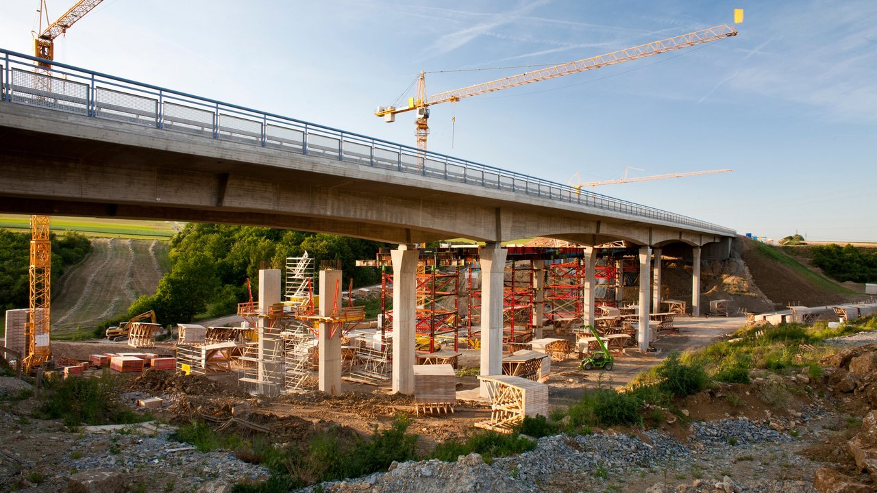 2 Kräne stehen hinter einer Brücke, die saniert werden soll