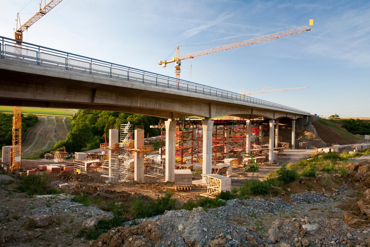 2 Kräne stehen hinter einer Brücke, die saniert werden soll