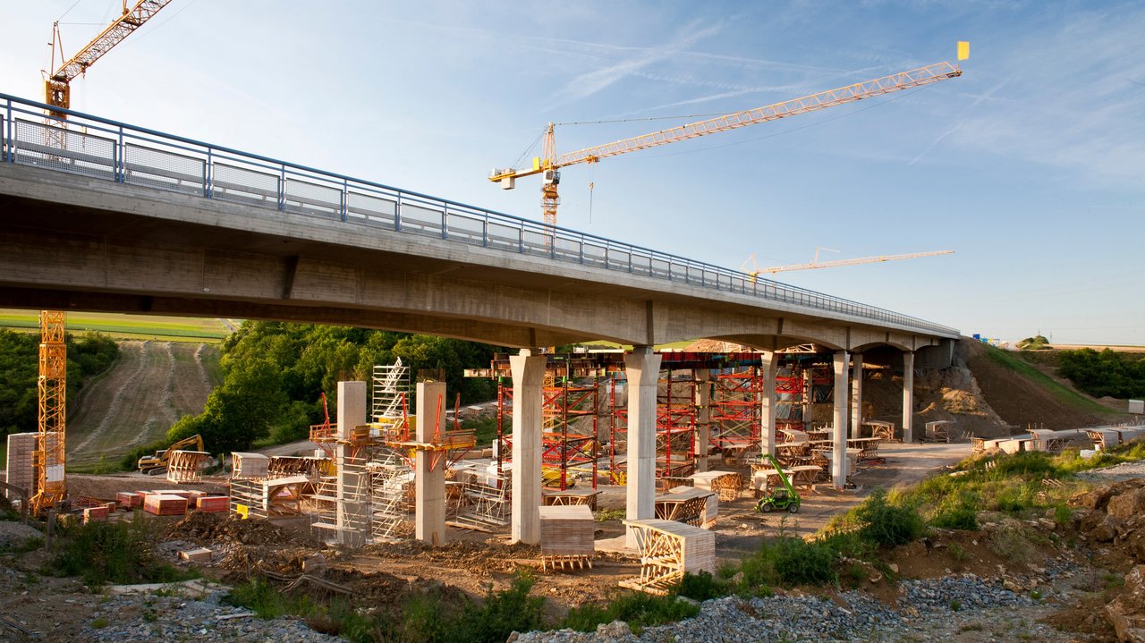 2 Kräne stehen hinter einer Brücke, die saniert werden soll