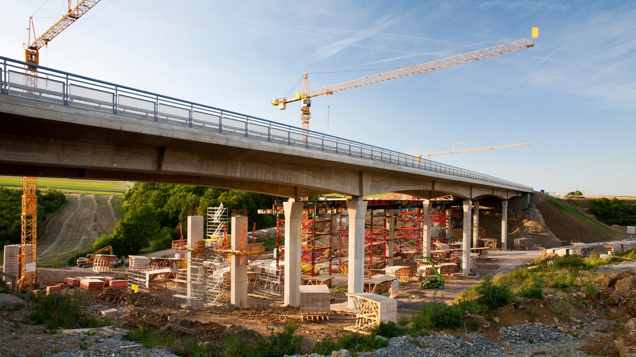 2 Kräne stehen hinter einer Brücke, die saniert werden soll
