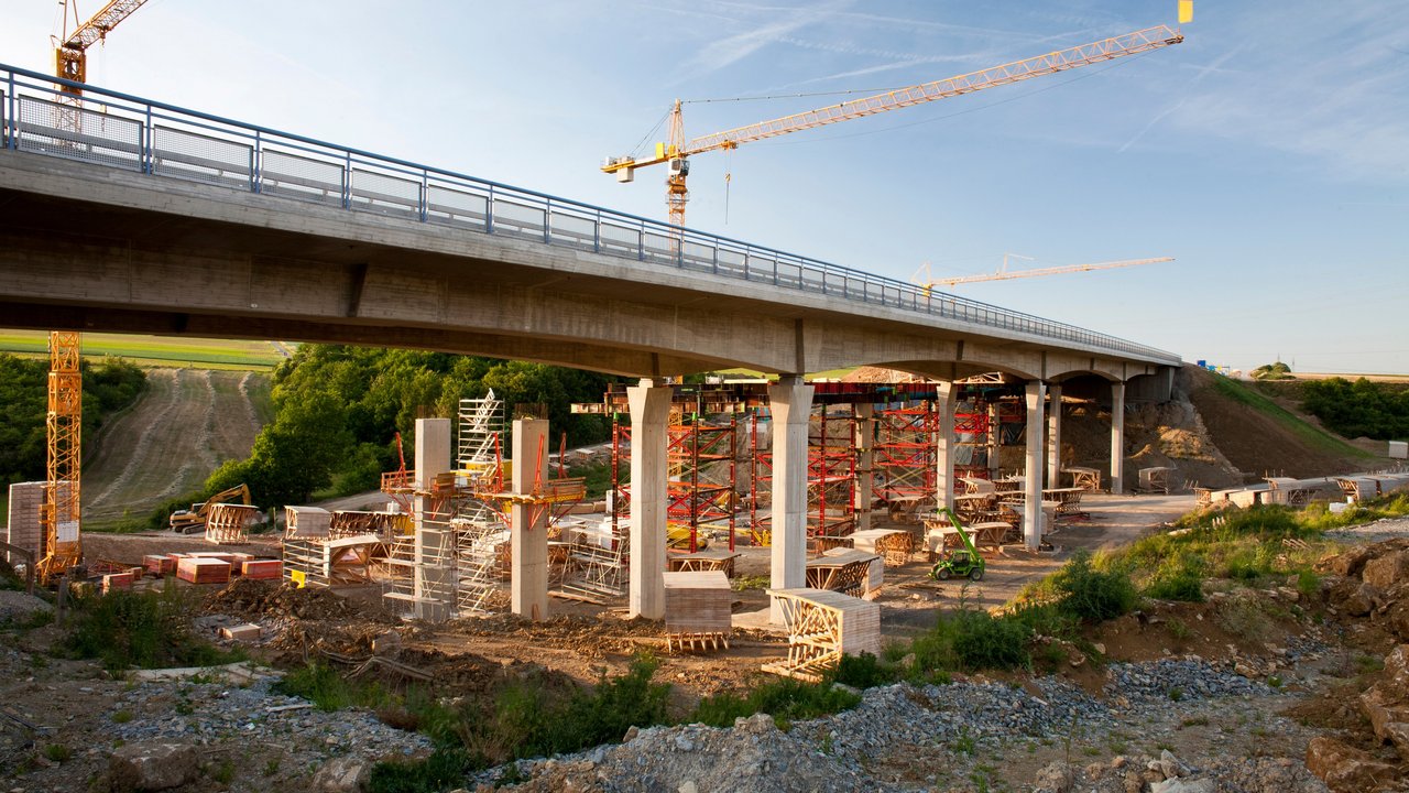2 Kräne stehen hinter einer Brücke, die saniert werden soll