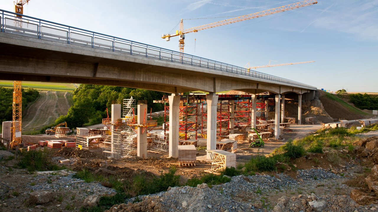 2 Kräne stehen hinter einer Brücke, die saniert werden soll