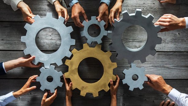 Bild zeigt Zahnräder mit Händen