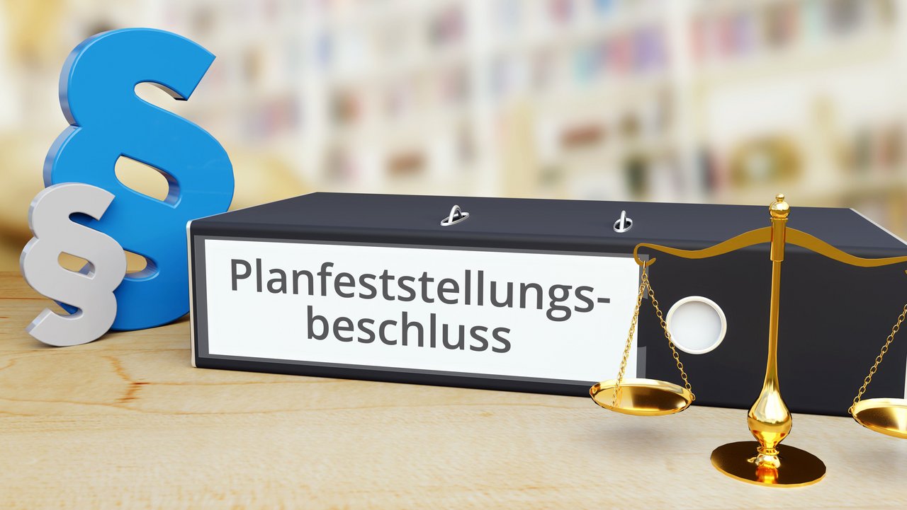 Aktenordner mit Beschriftung Planfeststellungsbeschluss, links daneben ein blaues und ein graues Paragraphenzeichen, rechts eine goldene Waage