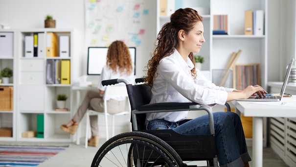 Bild zeigt Frau im Rollstuhl die im Büro am Laptop arbeitet