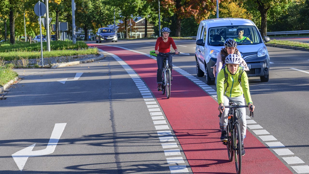 Radfahrer auf einem rot gekennzeichneten Radweg, im Hintergrund ein Auto