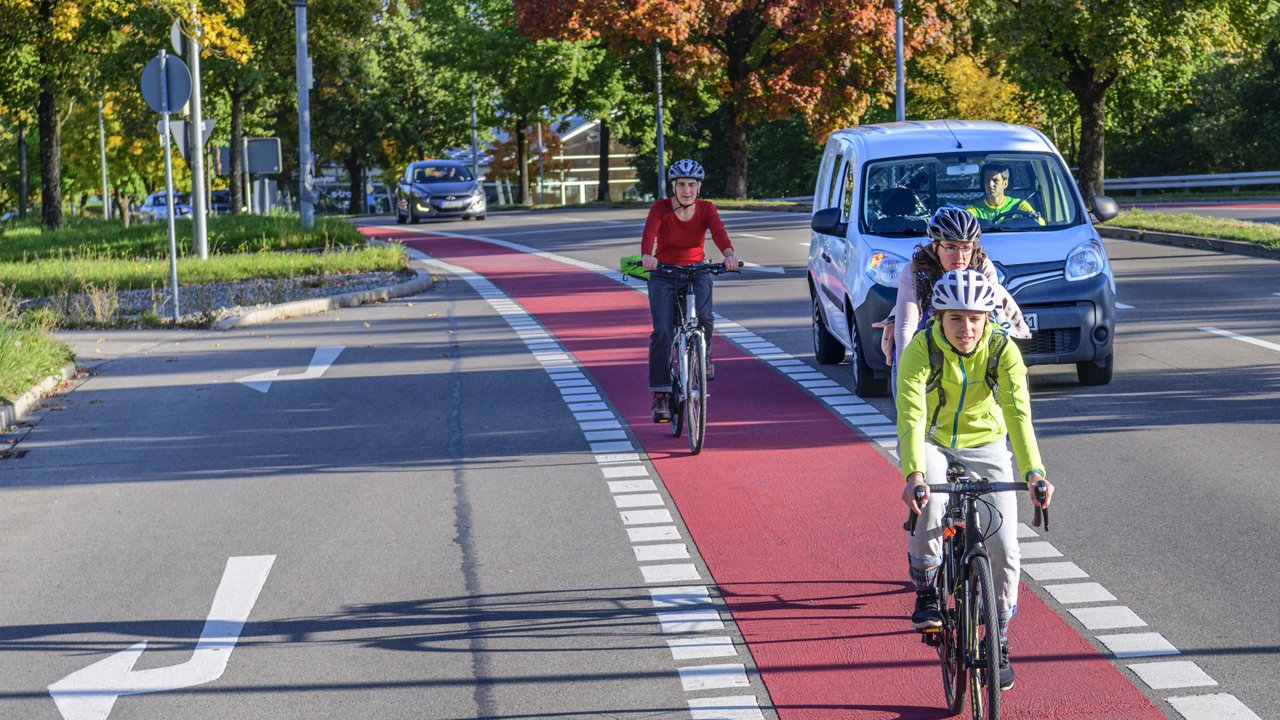 Radfahrer auf einem rot gekennzeichneten Radweg, im Hintergrund ein Auto