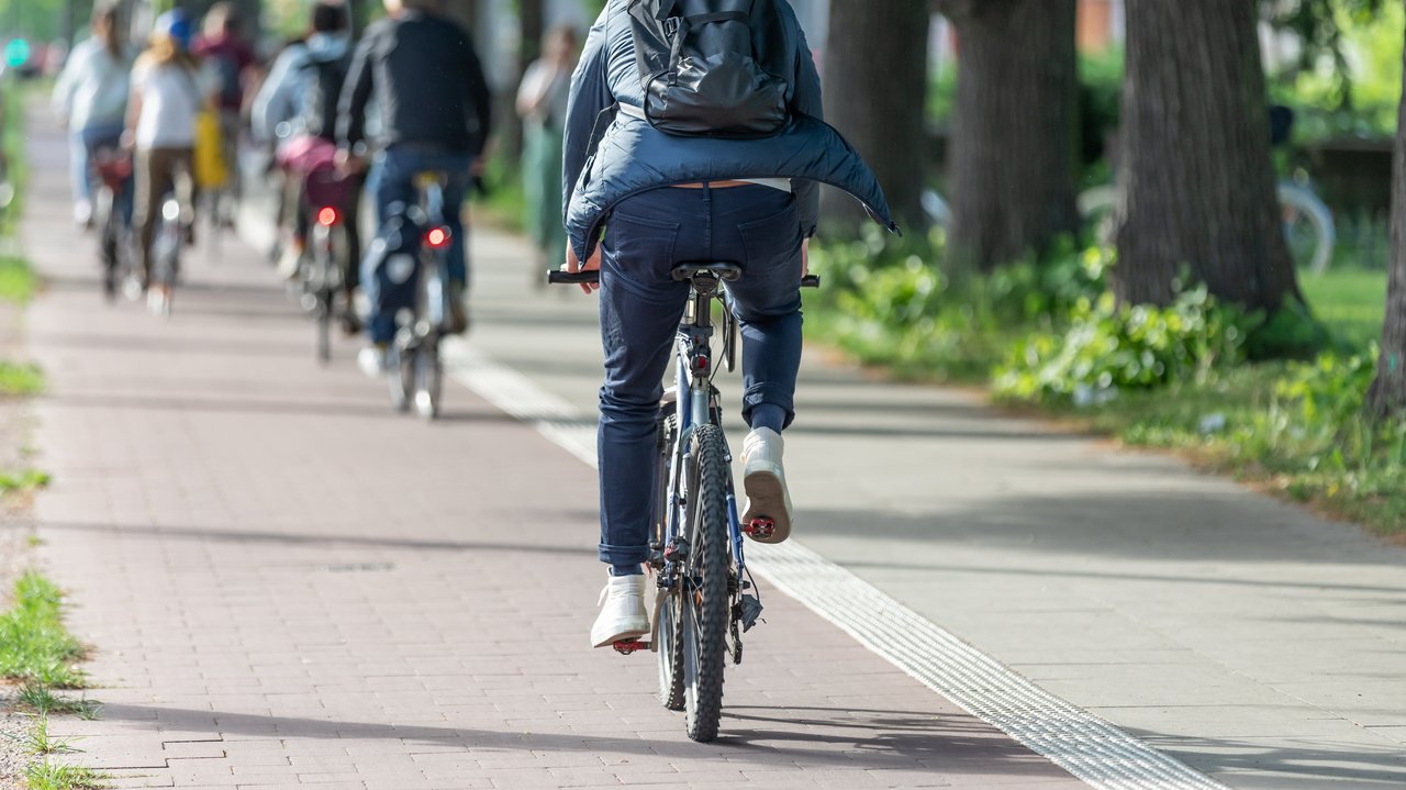 Bild zeigt Rückansicht eines Fahrradfahres mit Rucksack auf einem Radweg