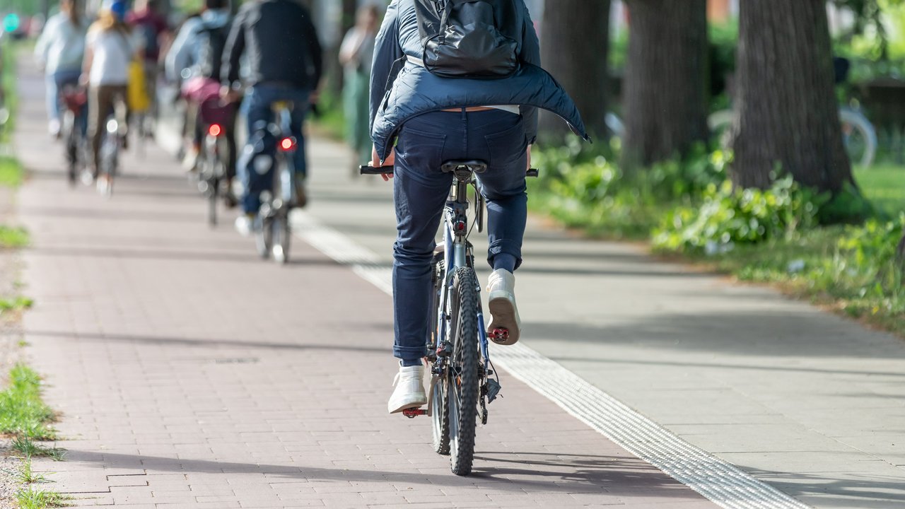 Bild zeigt Rückansicht eines Fahrradfahres mit Rucksack auf einem Radweg