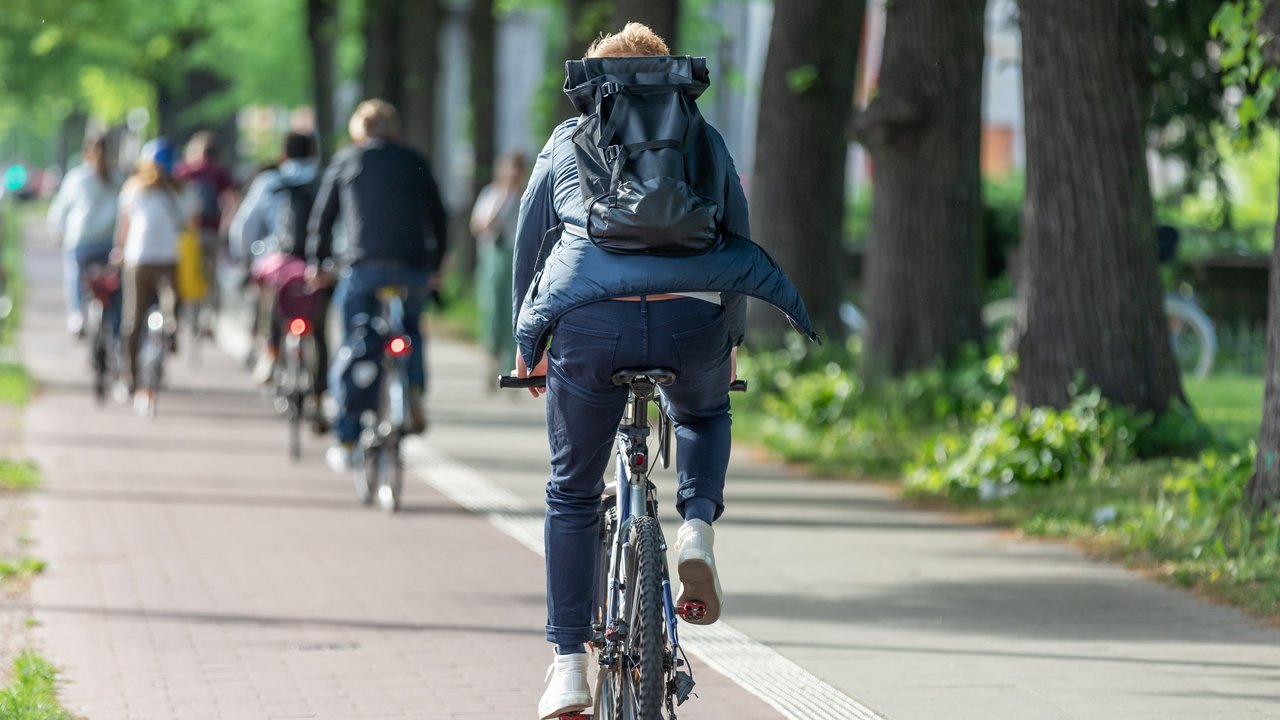 Bild zeigt Rückansicht eines Fahrradfahres mit Rucksack auf einem Radweg