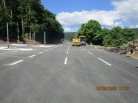 Straße auf der zwei Baufahrzeuge stehen, rechts und links stehen Bäume