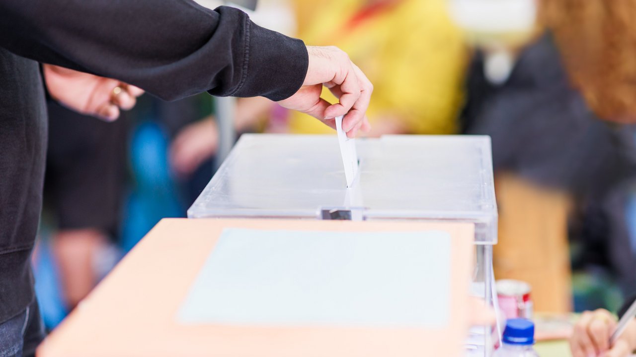 Das Foto zeigt eine Person, die einen Umschlag in eine Wahlurne steckt