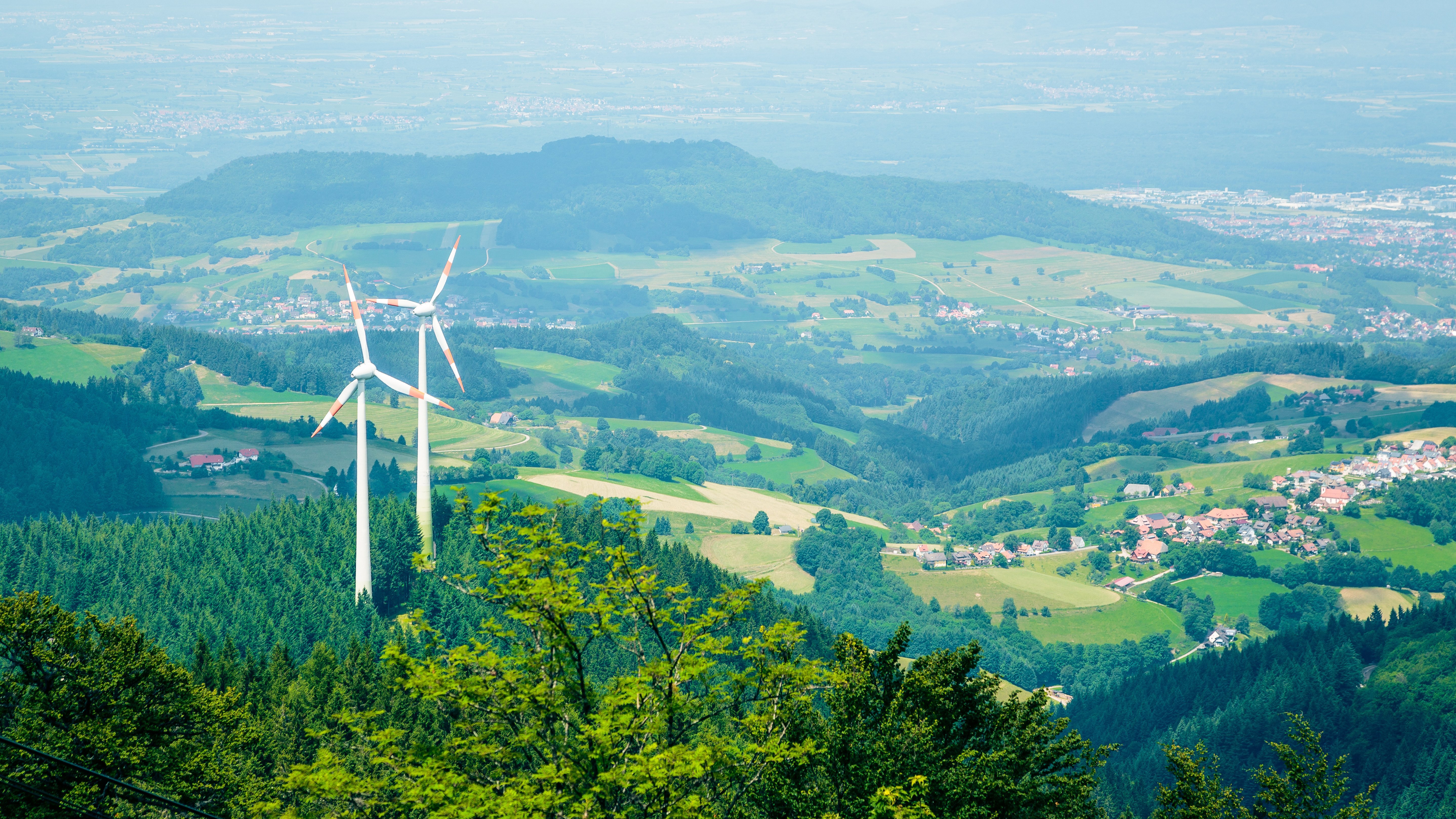 Man blickt von oben auf zwei Windenergieanlagen, die im Wald auf dem Berg Schauinsland stehen.
