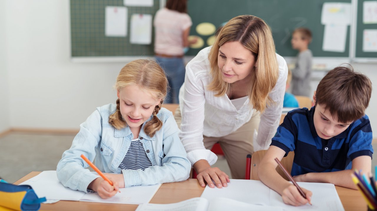 Bild zeigt Lehrerin, die zwei jüngeren Schülern im Unterricht etwas erklärt