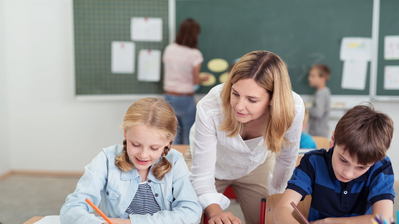 Bild zeigt Lehrerin, die zwei jüngeren Schülern im Unterricht etwas erklärt