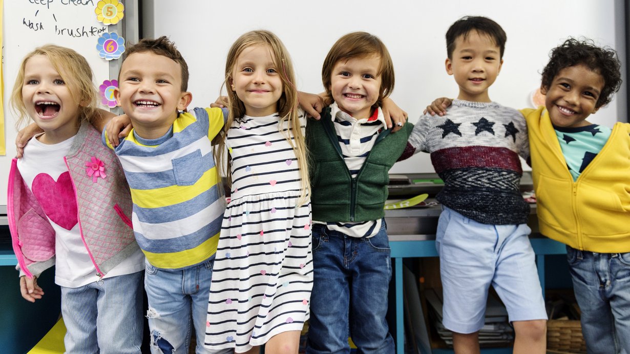 glückliche Grundschulkinder stehen umarmt in Reihe