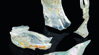 Aus dem römischen Neuenstadt am Kocher stammt ein aufwändig gearbeiteter, luxuriöser Glaskrug mit Kettenhenkel und verziertem Gefäßkörper, der durch einen Brand verformt ist. 