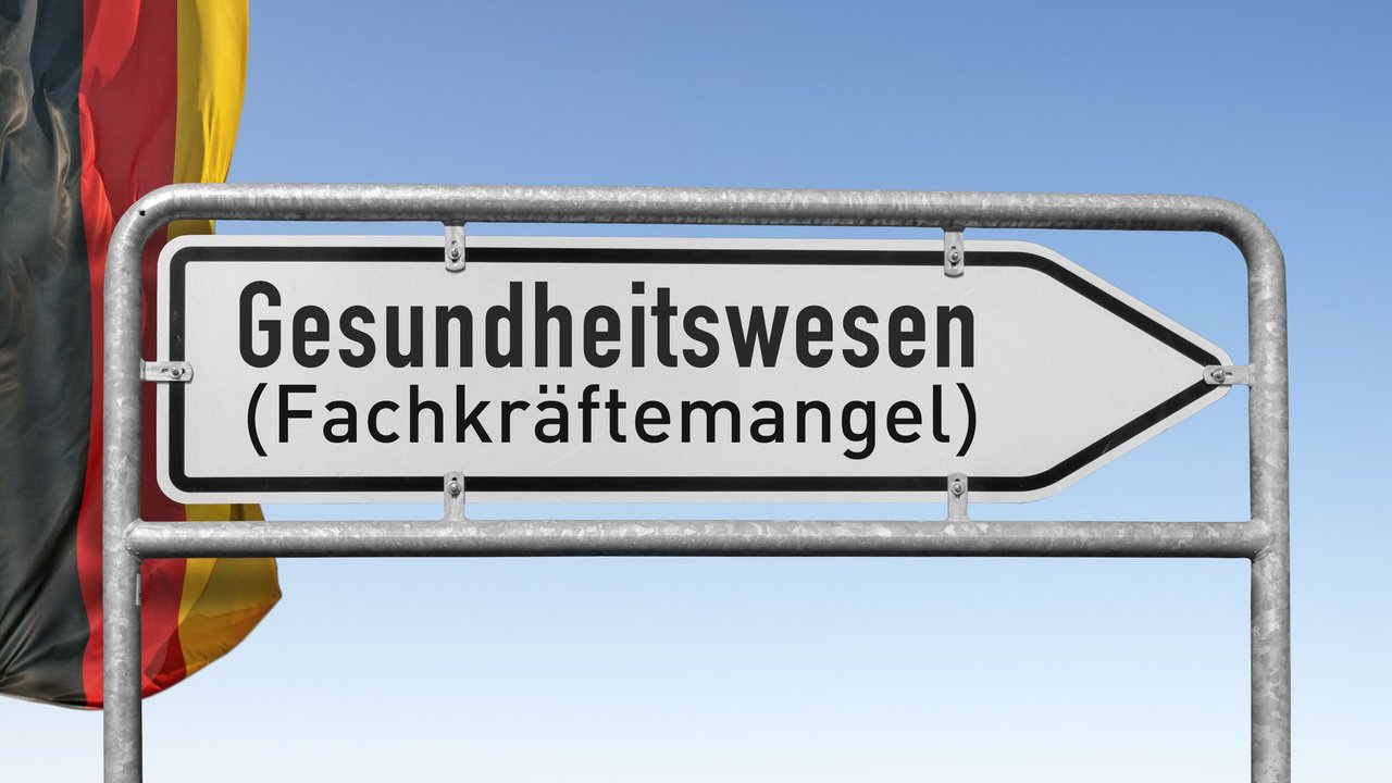 Wegweiser mit Schriftzug Gesundheitswesen (Fachkräftemangel), links daneben eine Deutschlandflagge